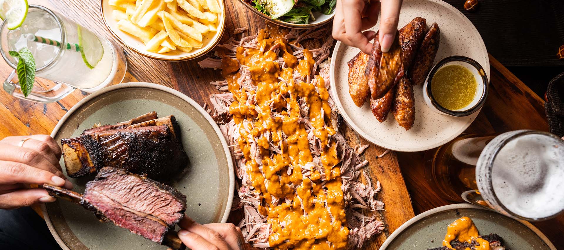 A loaded TBBQ spread: sliced brisket, pork ribs, wings and sides on butcher paper