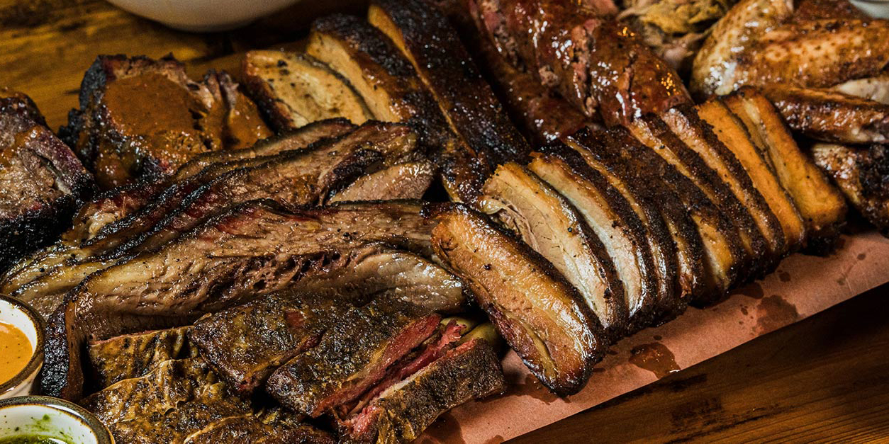 Platter of sliced brisket, ribs, pork belly and smoked chicken on butcher paper
